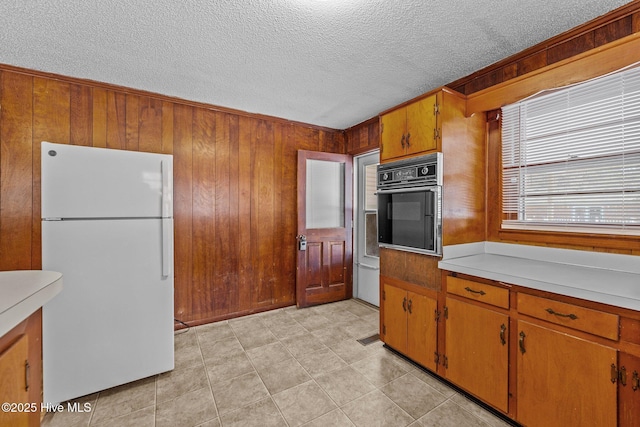 kitchen featuring wooden walls, brown cabinets, freestanding refrigerator, light countertops, and black oven