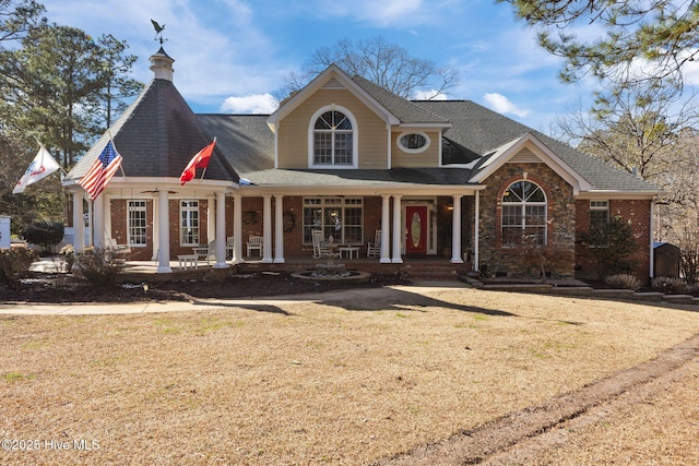 view of front of home with brick siding, a front lawn, a porch, and a shingled roof