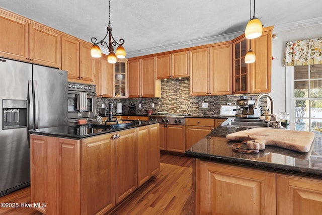 kitchen featuring wood finished floors, a sink, appliances with stainless steel finishes, decorative backsplash, and pendant lighting