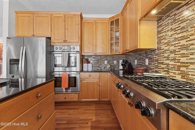 kitchen with decorative backsplash, custom range hood, glass insert cabinets, wood finished floors, and stainless steel appliances