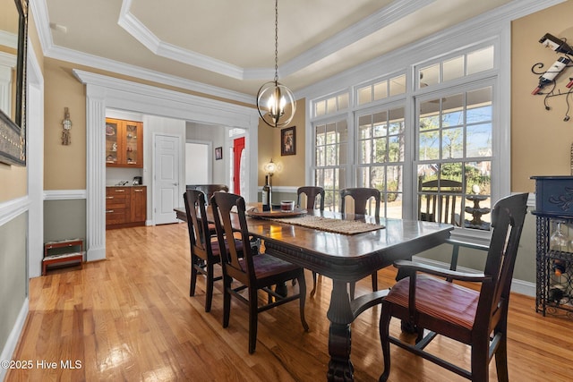 dining room featuring ornamental molding, a tray ceiling, plenty of natural light, and light wood-style floors