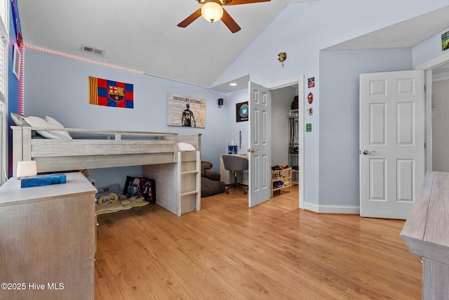 bedroom featuring visible vents, baseboards, light wood-style flooring, a walk in closet, and vaulted ceiling