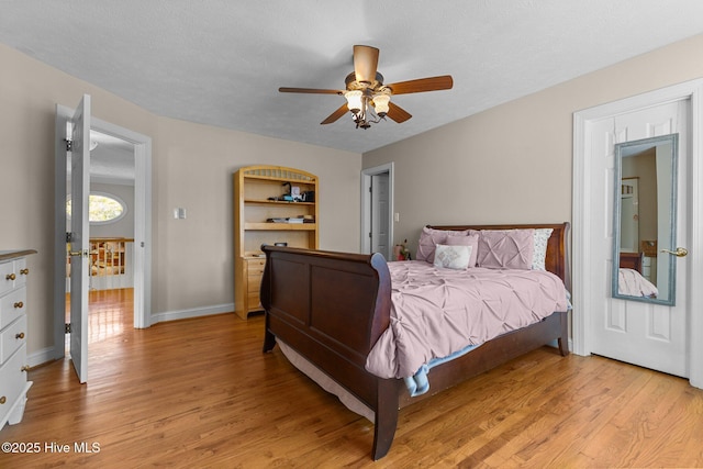 bedroom featuring a textured ceiling, light wood-type flooring, a ceiling fan, and baseboards