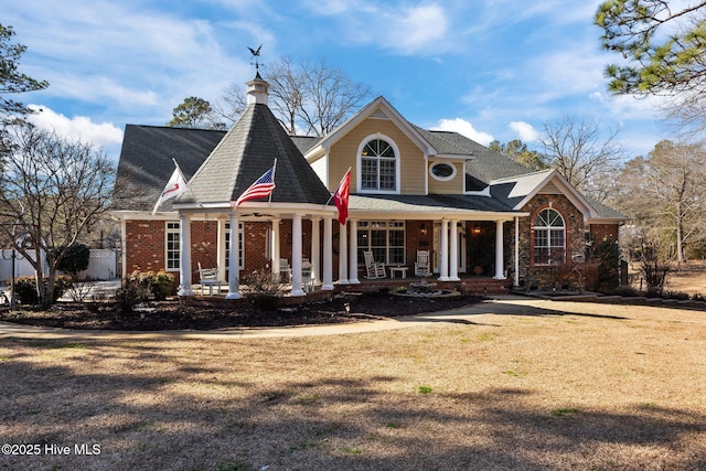 view of front of house with covered porch, brick siding, and a front lawn