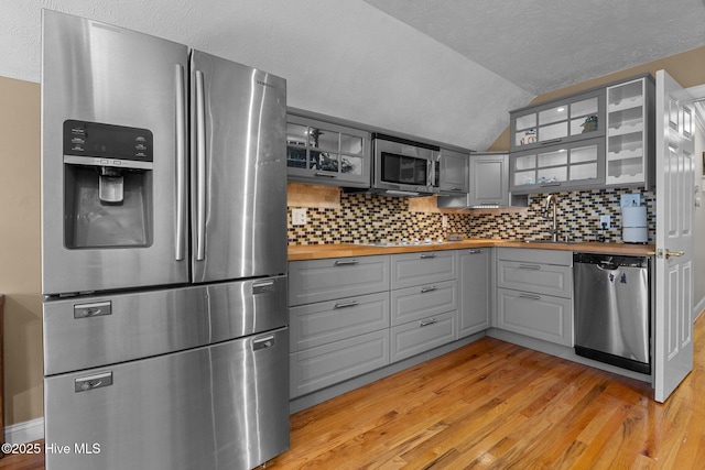 kitchen with stainless steel appliances, gray cabinets, a sink, wood counters, and light wood-type flooring