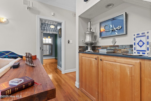 bar with light wood-type flooring, crown molding, and baseboards