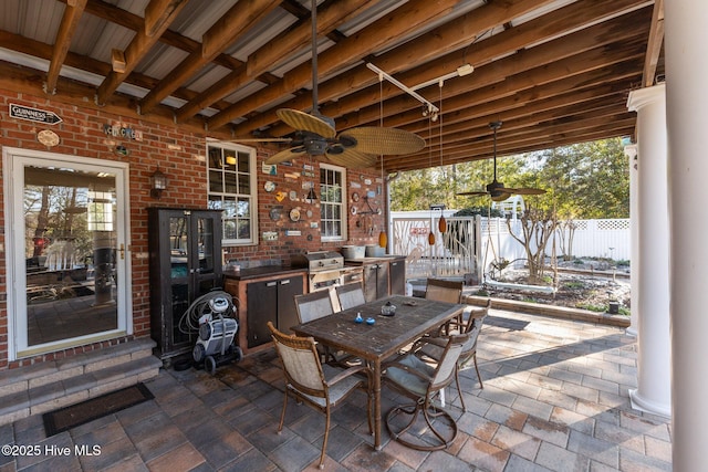 view of patio / terrace featuring grilling area, a ceiling fan, outdoor dining space, fence, and exterior kitchen