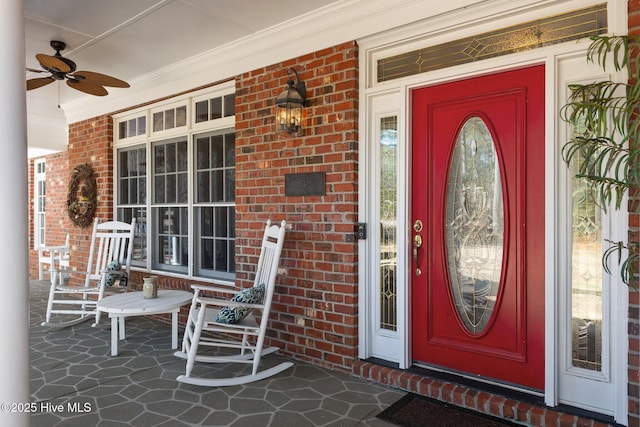 doorway to property featuring a ceiling fan, covered porch, and brick siding