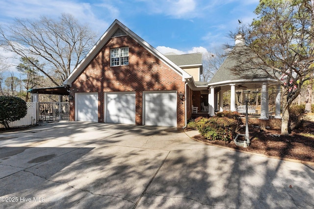 view of side of home featuring driveway, covered porch, an attached garage, and brick siding