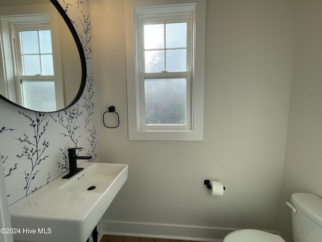 half bath with a wealth of natural light, a sink, toilet, and baseboards