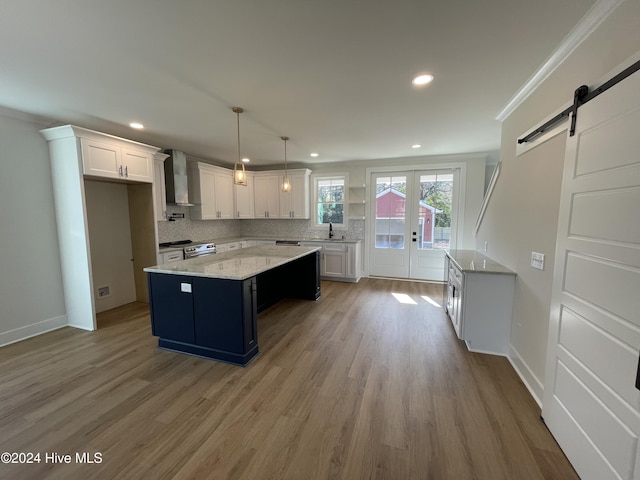 kitchen featuring a barn door, wall chimney exhaust hood, backsplash, stainless steel range with electric stovetop, and a sink