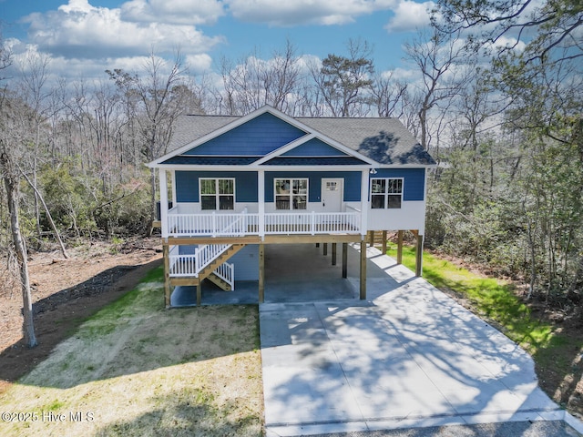 coastal inspired home with a carport, a porch, roof with shingles, and concrete driveway