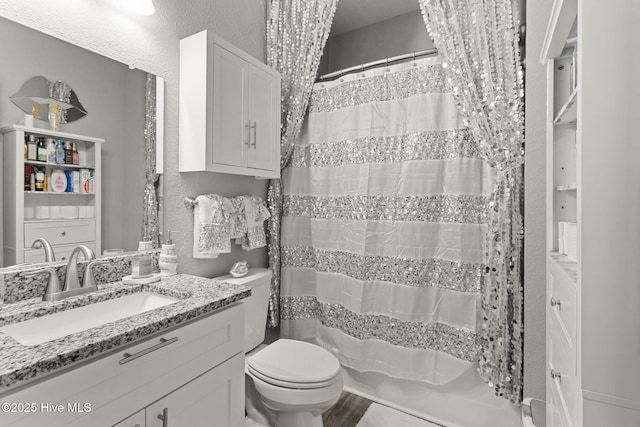 full bathroom with toilet, curtained shower, vanity, and a textured wall