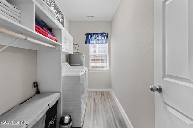 laundry room with light wood finished floors, cabinet space, washing machine and dryer, electric water heater, and baseboards