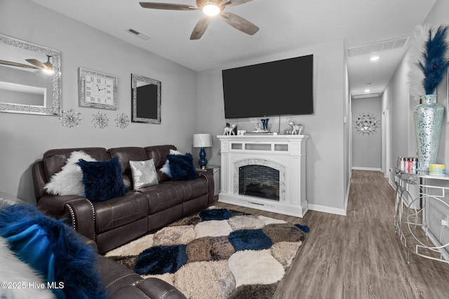 living area with a ceiling fan, wood finished floors, visible vents, and a premium fireplace