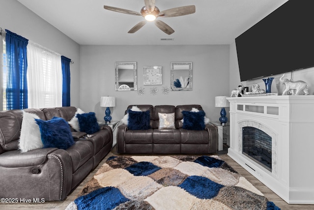 living room featuring ceiling fan, a fireplace, wood finished floors, and visible vents