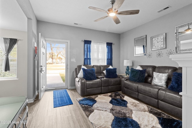 living area with a ceiling fan, visible vents, baseboards, and wood finished floors