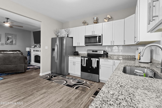 kitchen featuring stainless steel appliances, a sink, white cabinets, open floor plan, and dark wood-style floors