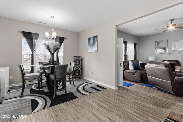 dining space with ceiling fan with notable chandelier, baseboards, and wood finished floors