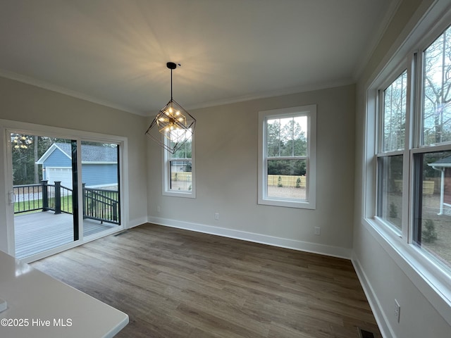 unfurnished dining area featuring dark wood-style floors, a notable chandelier, crown molding, and baseboards