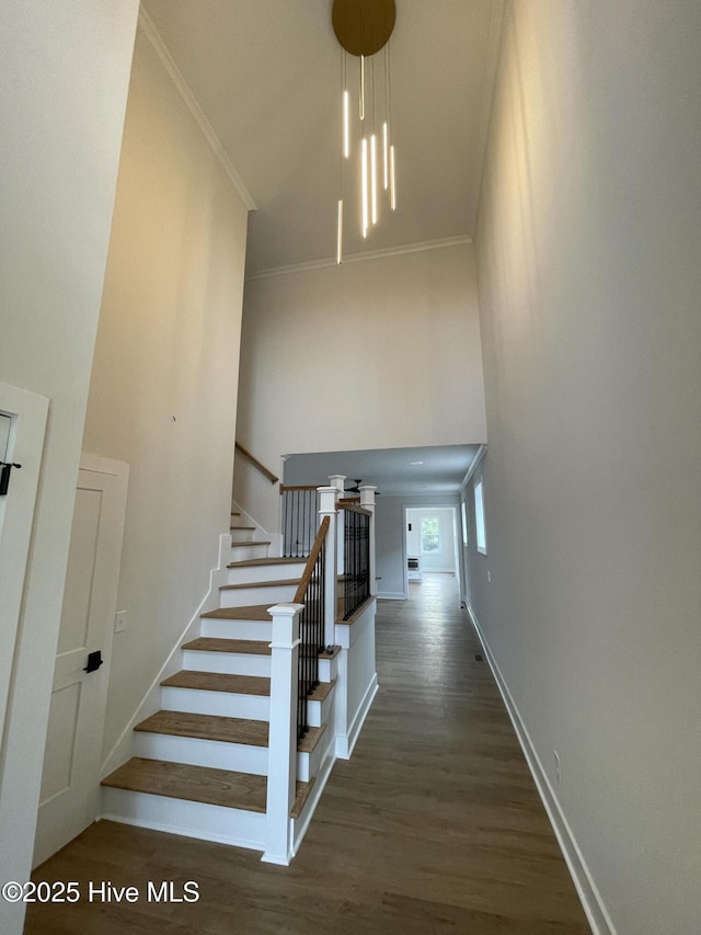 stairway featuring wood finished floors, a towering ceiling, and crown molding