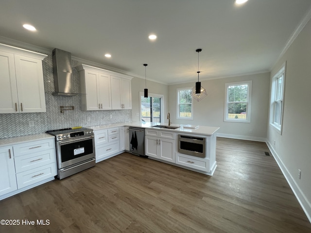 kitchen with stainless steel appliances, a peninsula, a sink, ornamental molding, and wall chimney range hood