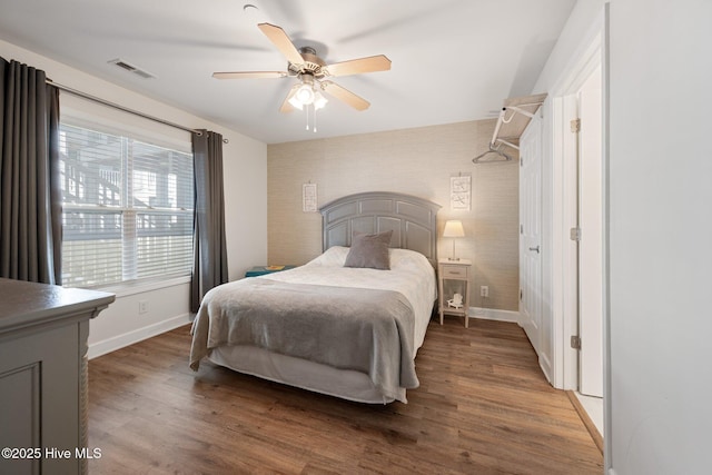 bedroom featuring a ceiling fan, baseboards, visible vents, and wood finished floors