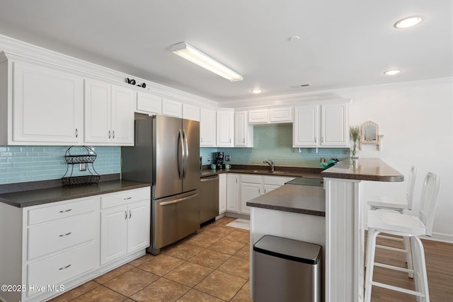 kitchen with stainless steel appliances, dark countertops, white cabinets, a sink, and a kitchen bar