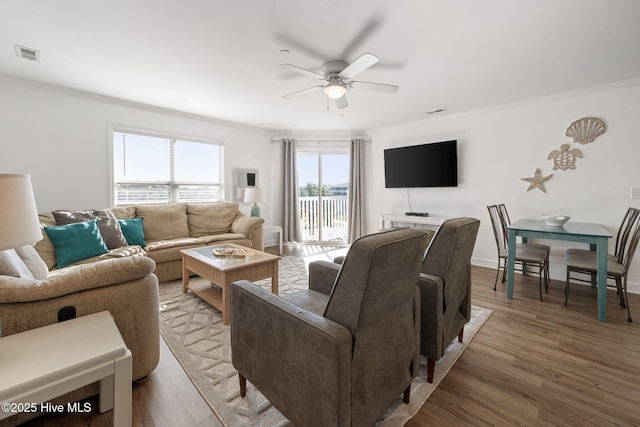 living area featuring crown molding, visible vents, a ceiling fan, wood finished floors, and baseboards