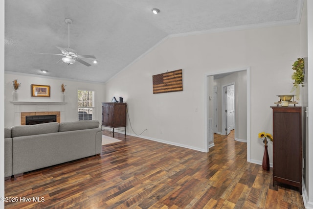 living area featuring wood finished floors, baseboards, a tile fireplace, vaulted ceiling, and crown molding