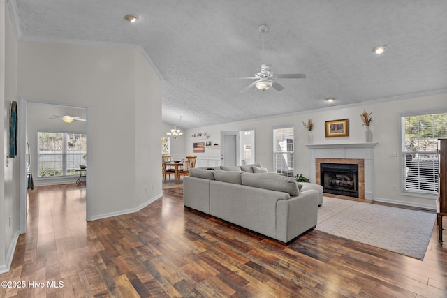 living area with a tiled fireplace, dark wood-style flooring, crown molding, and vaulted ceiling