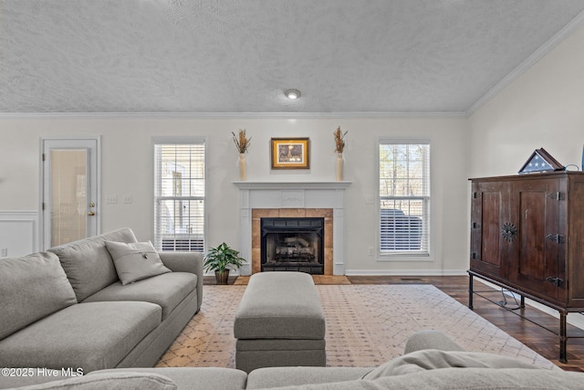 living area with a healthy amount of sunlight, a tile fireplace, a textured ceiling, and crown molding