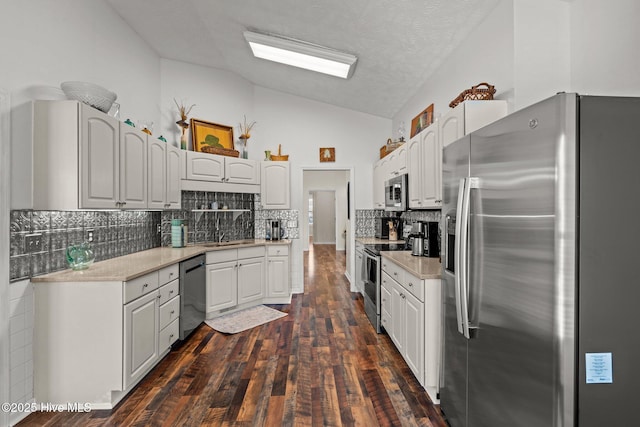 kitchen with dark wood-type flooring, a sink, stainless steel appliances, light countertops, and lofted ceiling