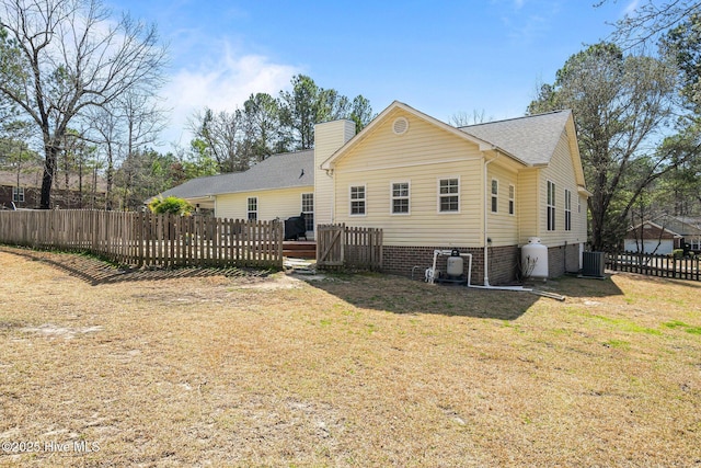 back of property with fence, a yard, central AC, a chimney, and a deck