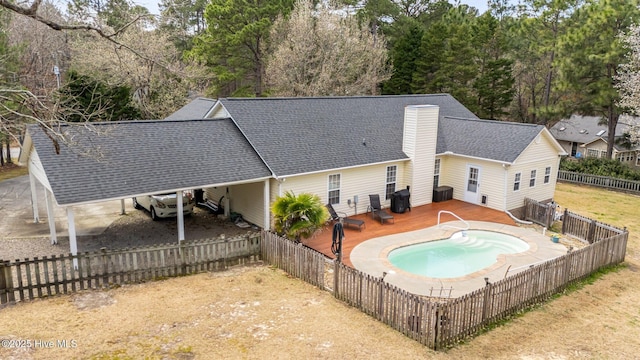 rear view of house with an attached carport, a shingled roof, a chimney, a deck, and a fenced backyard