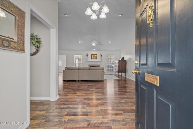 foyer with baseboards, vaulted ceiling, ceiling fan with notable chandelier, a fireplace, and dark wood-style floors