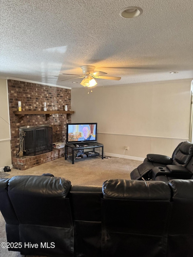 carpeted living area with a wainscoted wall, a textured ceiling, a fireplace, and a ceiling fan