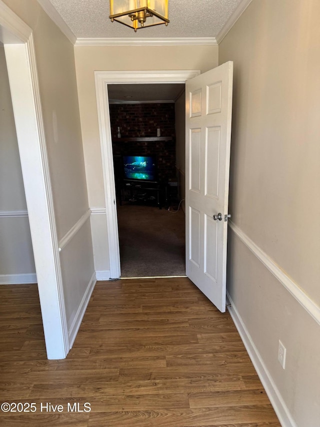 hall with a textured ceiling, ornamental molding, wood finished floors, and baseboards