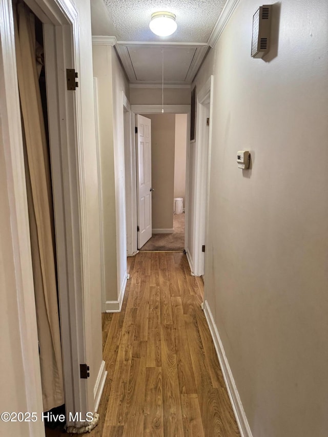 corridor featuring crown molding, attic access, a textured ceiling, wood finished floors, and baseboards