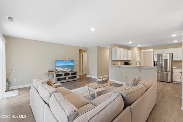 living room featuring light wood finished floors, recessed lighting, visible vents, and baseboards