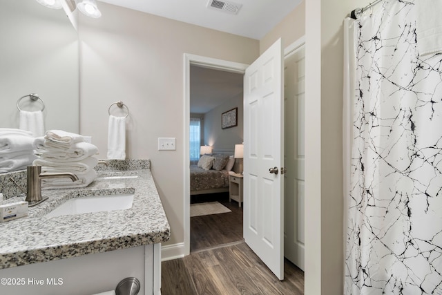 ensuite bathroom with ensuite bathroom, a shower with shower curtain, wood finished floors, vanity, and visible vents