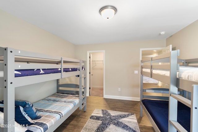 bedroom featuring wood finished floors, a walk in closet, and baseboards