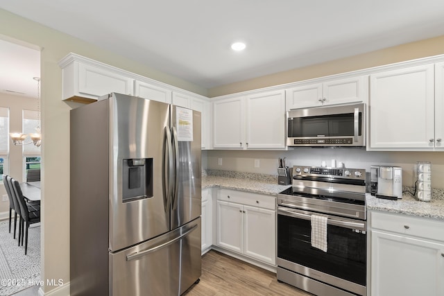 kitchen with light wood finished floors, white cabinets, light stone countertops, stainless steel appliances, and a notable chandelier