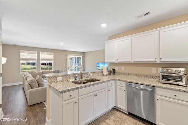 kitchen with open floor plan, a peninsula, stainless steel dishwasher, white cabinetry, and a sink