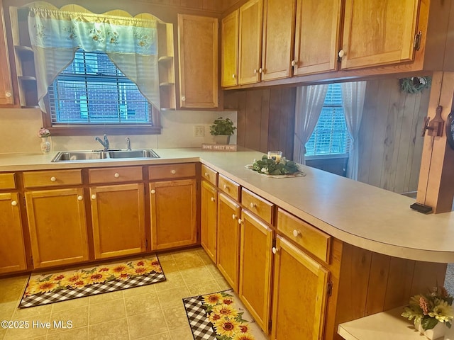 kitchen with brown cabinetry, light countertops, a sink, and a peninsula