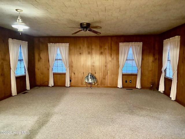 carpeted spare room featuring a ceiling fan, visible vents, and wooden walls