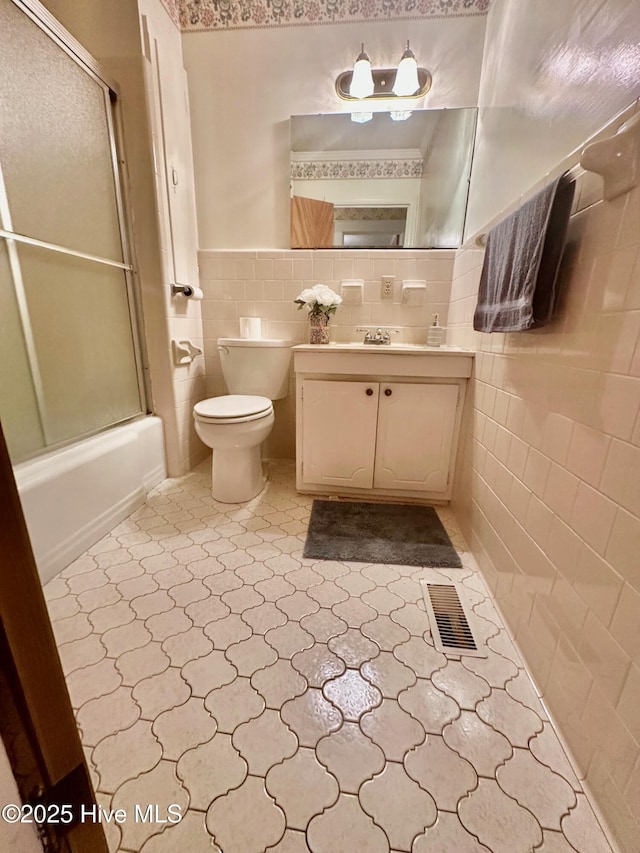 full bath featuring visible vents, toilet, shower / bath combination with glass door, vanity, and tile walls