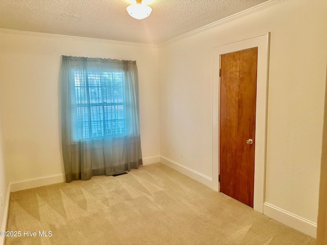 carpeted empty room featuring a textured ceiling, baseboards, and crown molding