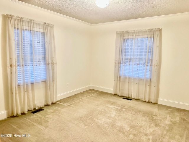 empty room featuring a textured ceiling, carpet, visible vents, and crown molding