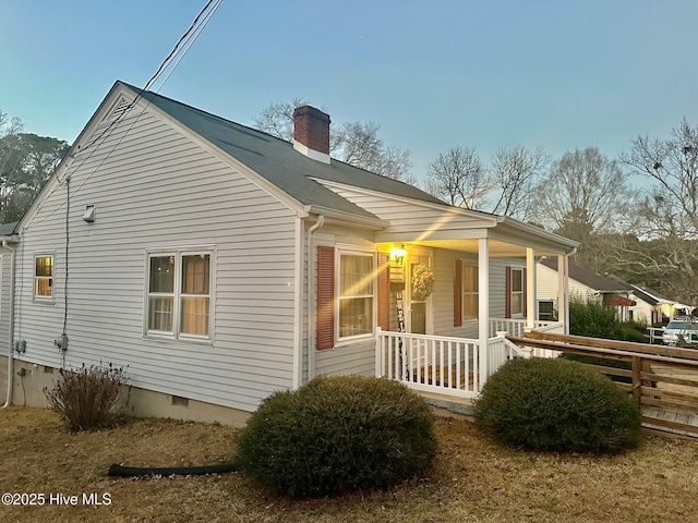 view of side of home with crawl space, covered porch, and a chimney